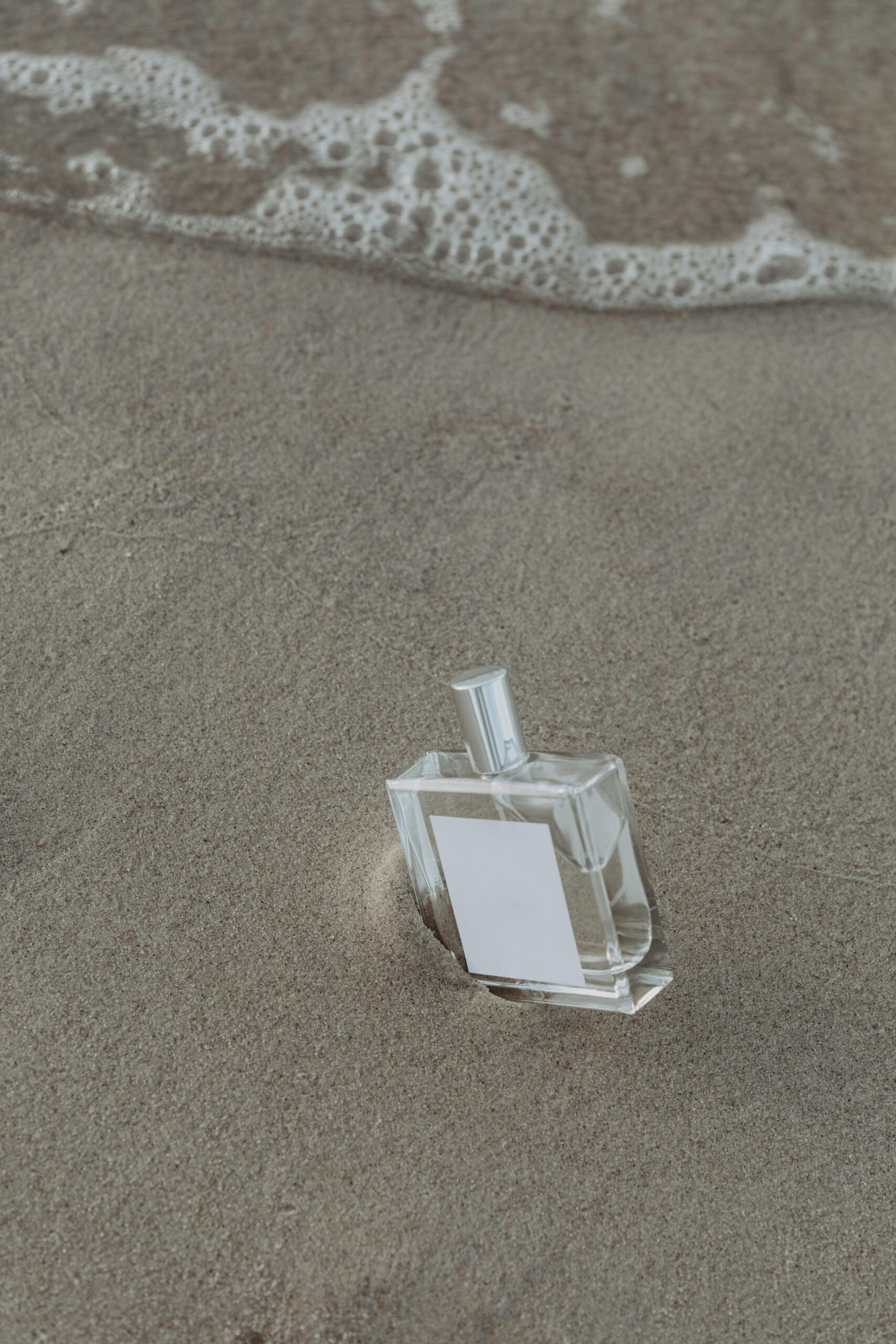 Elegant perfume bottle displayed on a sandy beach with calming waves, perfect for product marketing.
